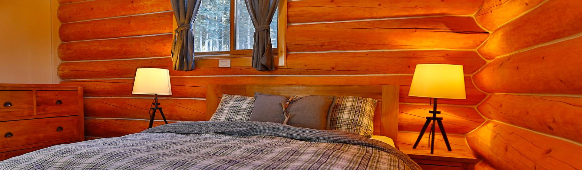 Panorama image of a queen size bed in one of the cabins with cozy lamps next to it