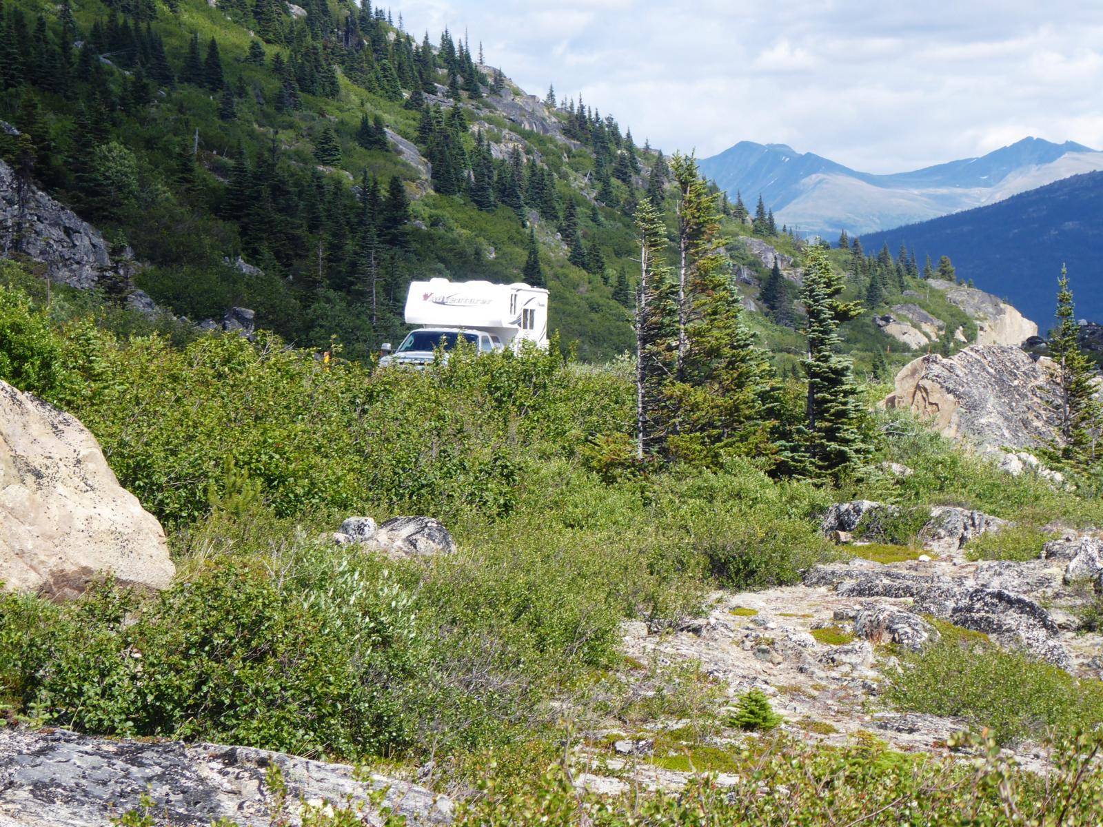 A campervan driving on a road through a wild and mountaineous path