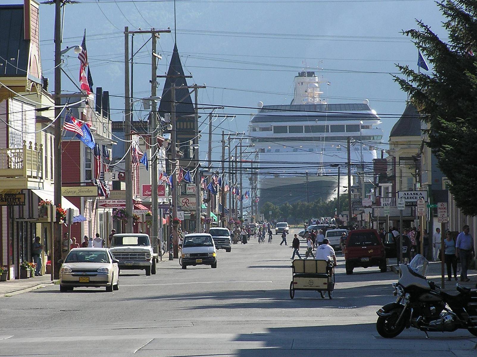 View along the main road in skagway towards the harbour with western style houses and a huge ship in the background