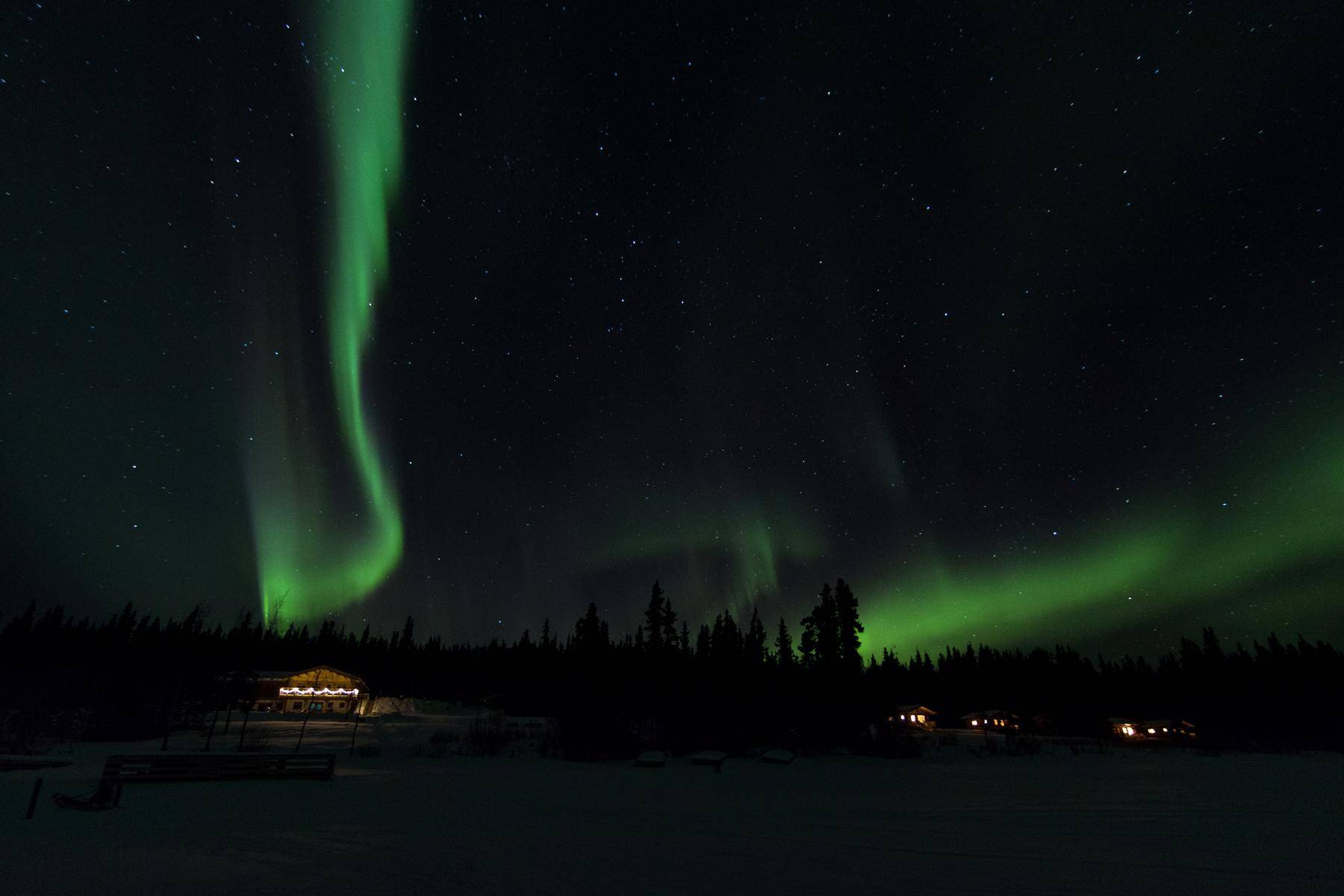 Northern lights over the property with lit cabins beneath it