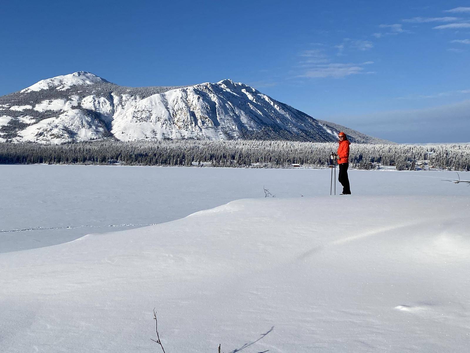 A woman on cross-country skis on the frozen tagish lake with large mountains in the background