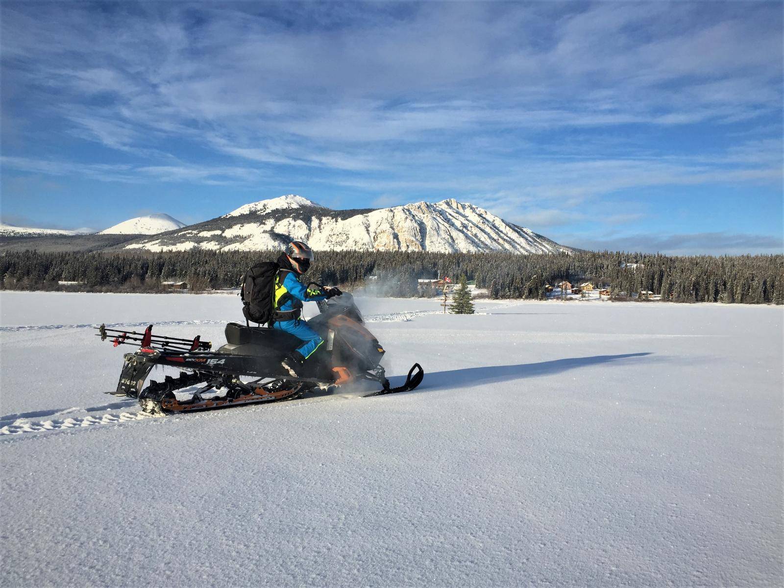 A man on a Skidoo driving over the frozen lake with snowy mountains in the back