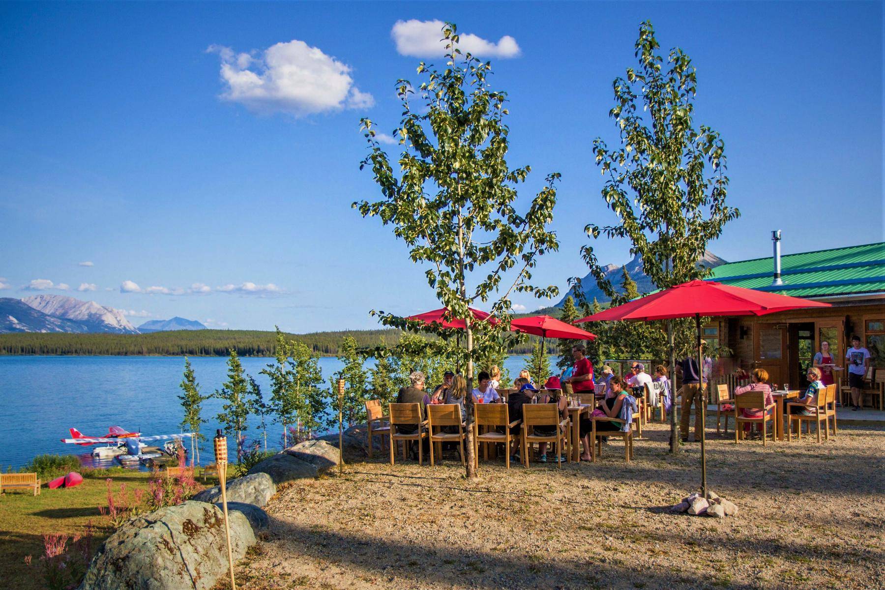 people eating on the garden patio with a float plane on the lake in the background in summer