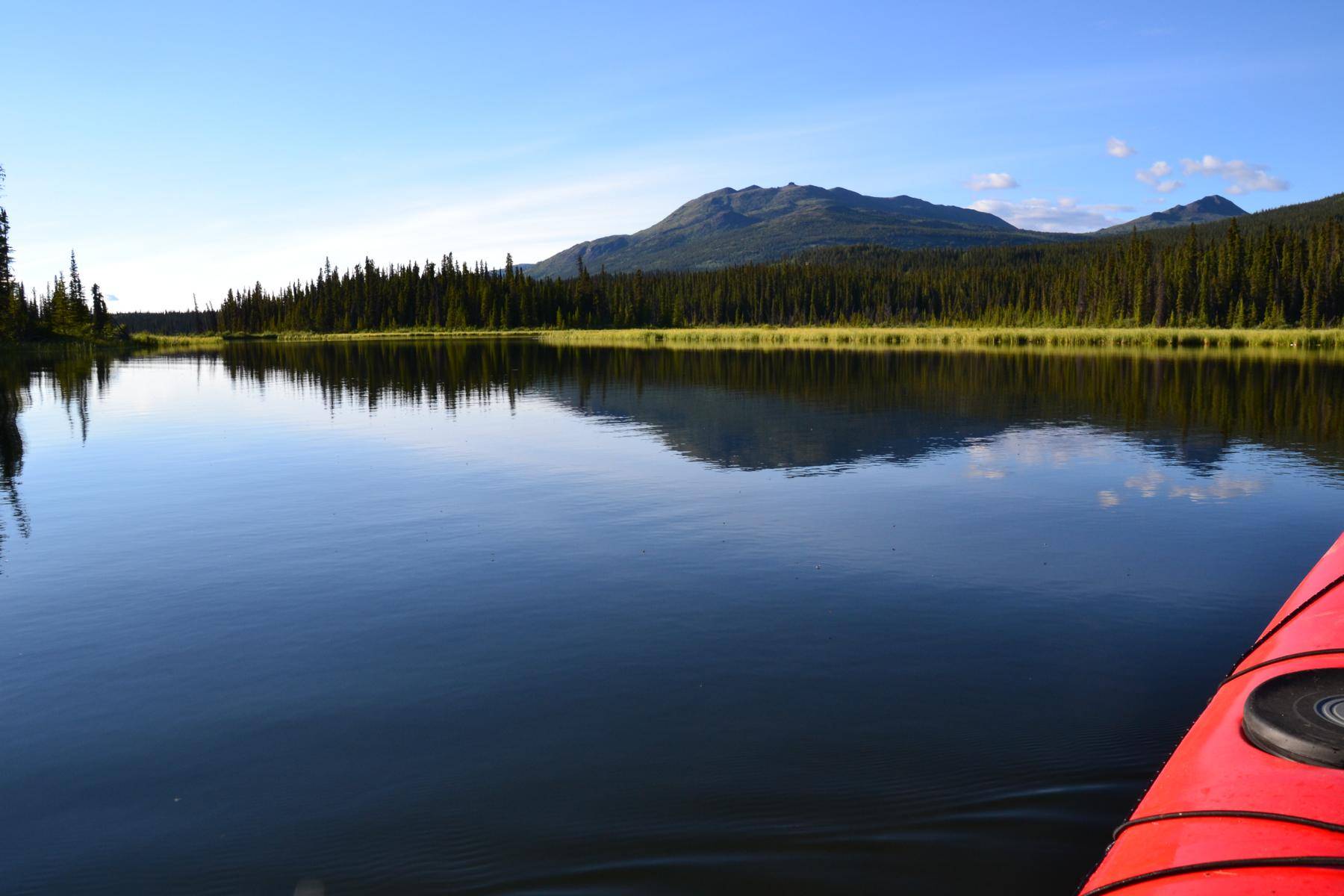 View from a kayak over the calm lake onto the mountains in the distance