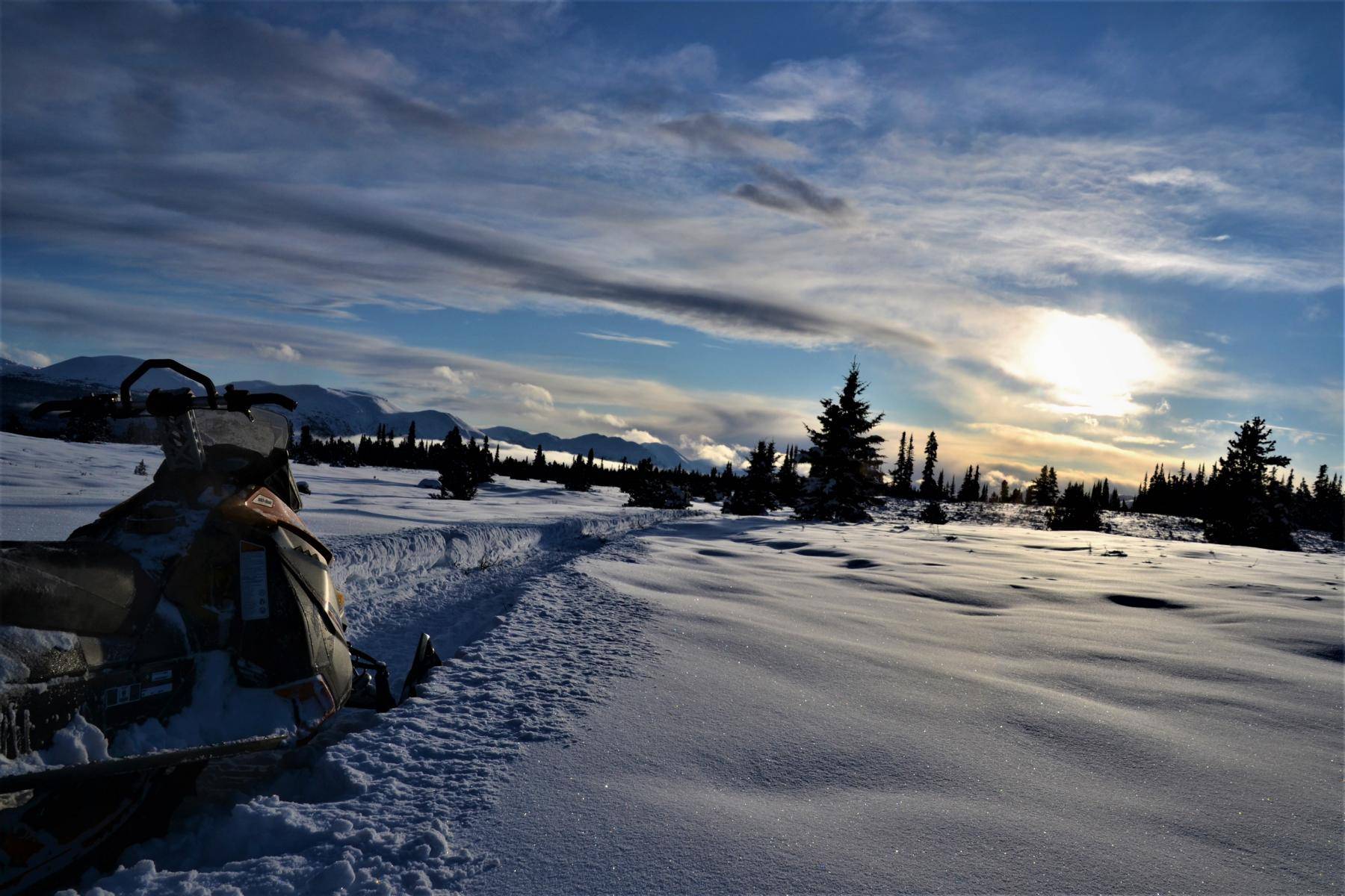 Sundown over a snowy landscape with a skidoo on a track in the foreground