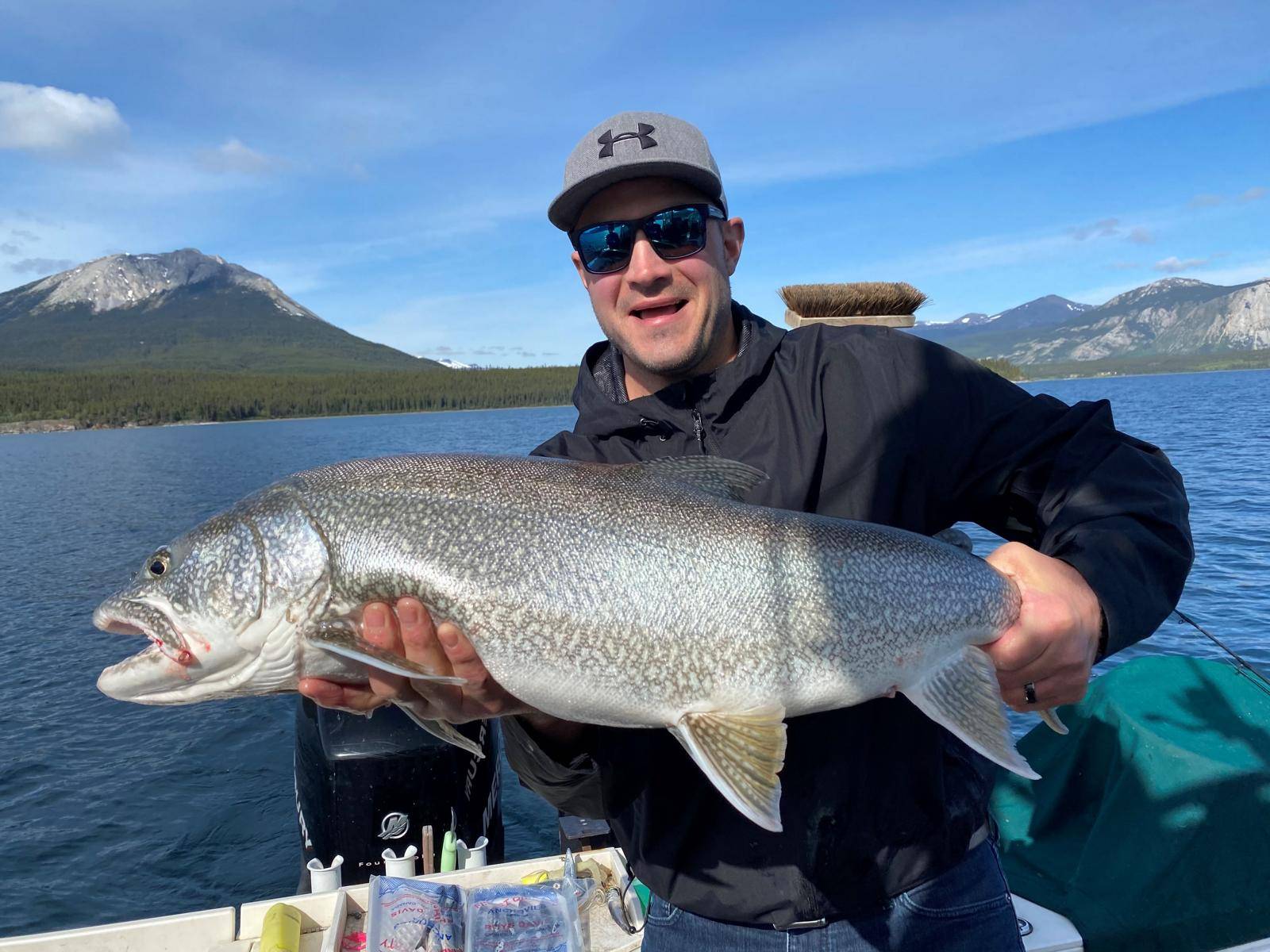 A man on a boat on a lake holding a large caught laketrout