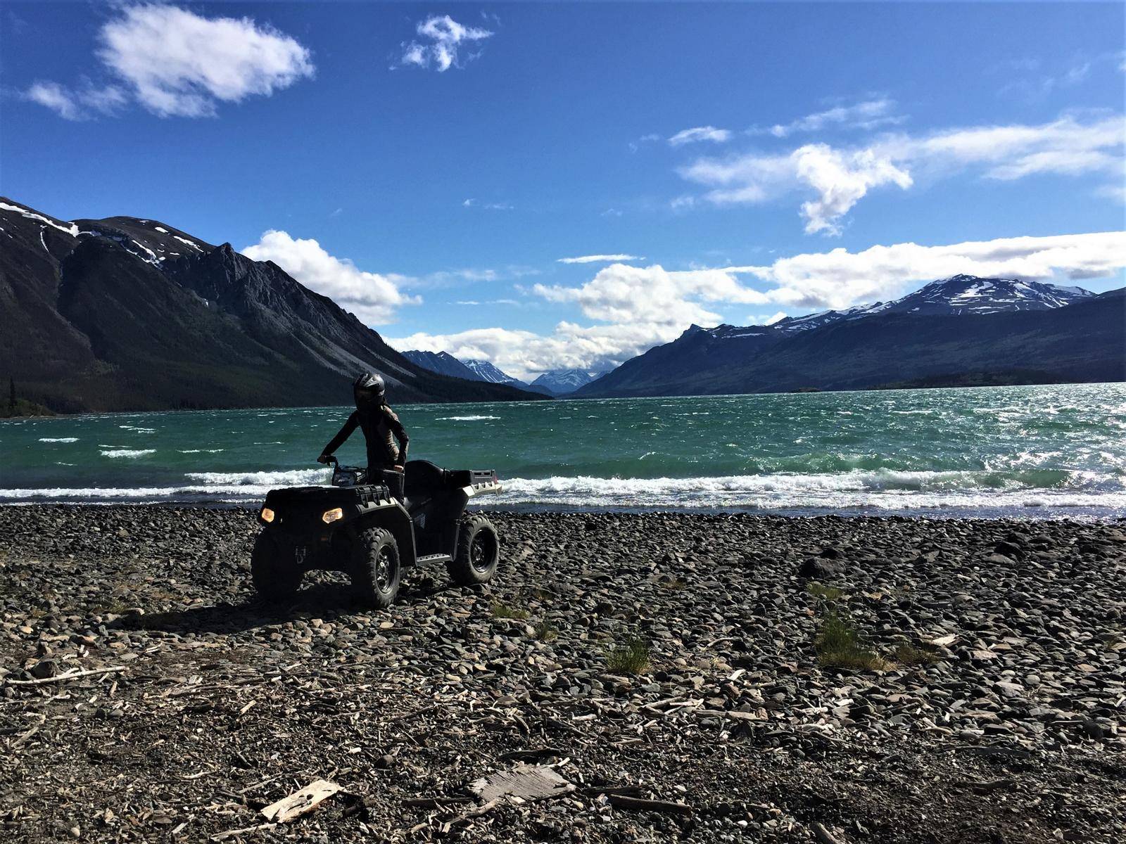 Person on ATV on shore of lake, mountains in back